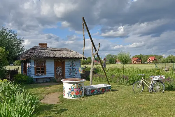Kolorowy dom malarek w Zalipiu, z kwiecistymi zdobieniami, studnią i rowerem.